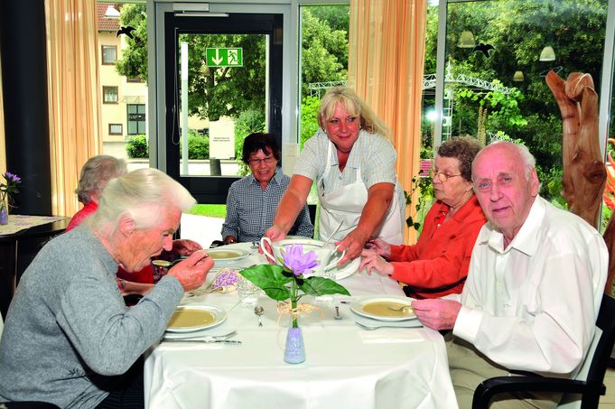 Pflegekraft serviert Senioren Suppe an gedecktem Tisch