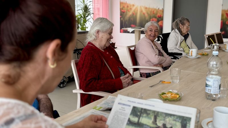 Gruppe sitzt um einen Tisch und liest Zeitung