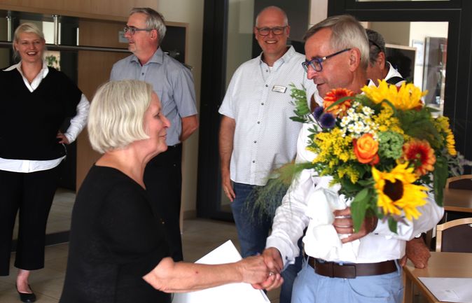 Älterer Mann mit Blumen schüttelt Hand einer Frau bei Wechsel im Stiftungsrat