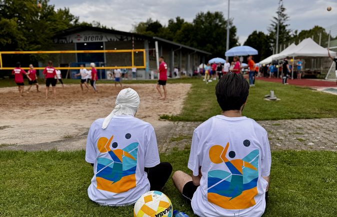 Zwei Personen in Veranstaltungs-T-Shirts sitzen und schauen Beachvolleyball