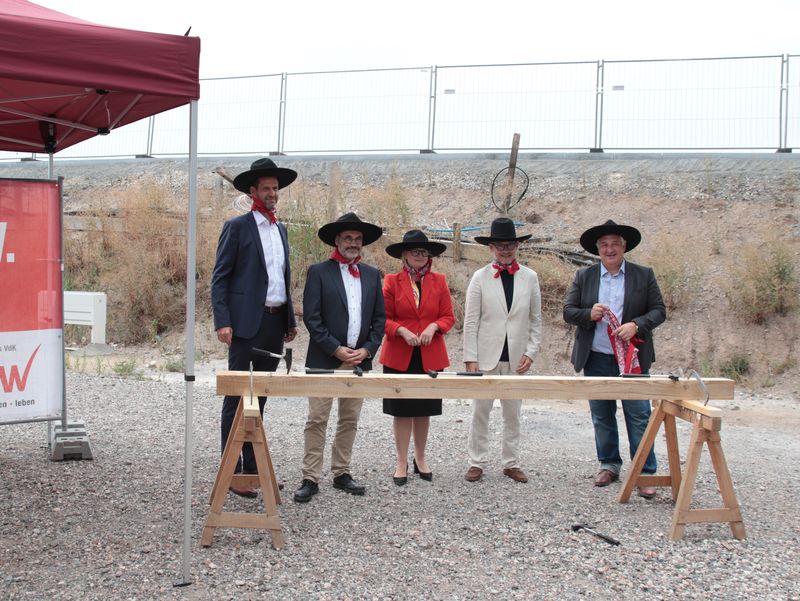 Teilnehmende mit schwarzen Hüten und roten Halstüchern posieren beim Richtfest auf der Baustelle.