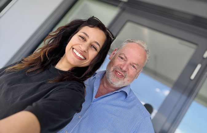 lächelnde Frau mit Mann im Hintergrund bei einem Selfie