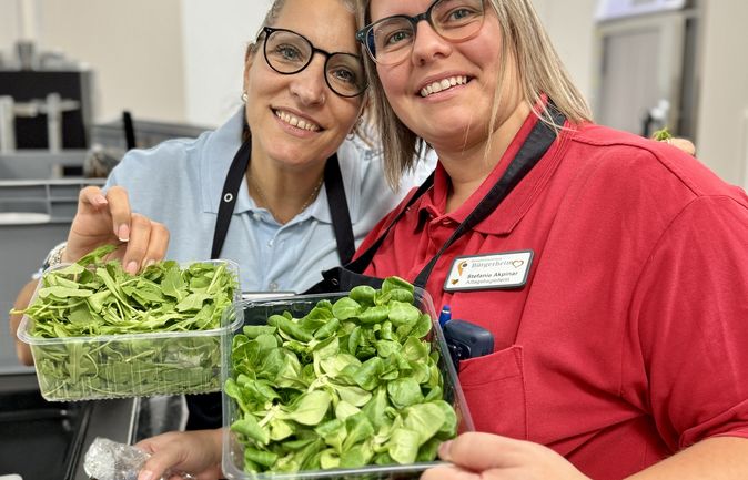 Zwei lächelnde Mitarbeitende beim Koch-Event mit Schüsseln frischer Salate