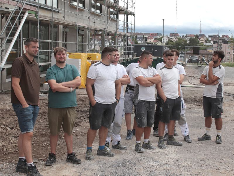 Handwerker stehen vor dem Neubau und verfolgen die Veranstaltung.