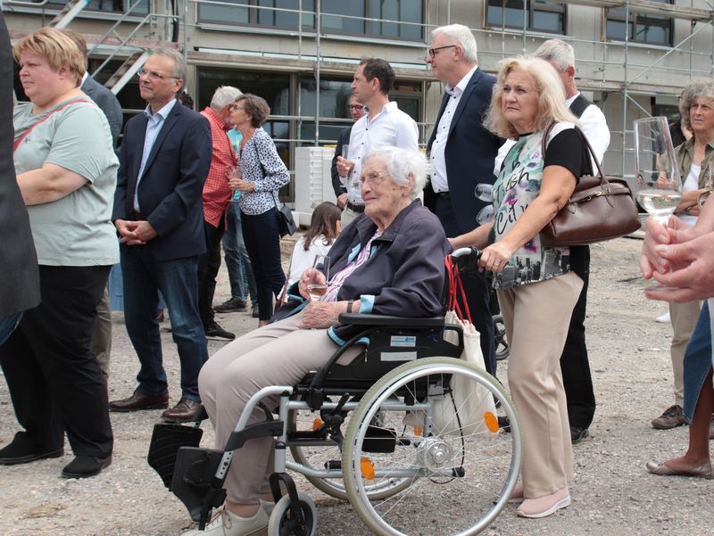 Besuchende stehen vor dem Neubau und nehmen an der Richtfestfeier teil.