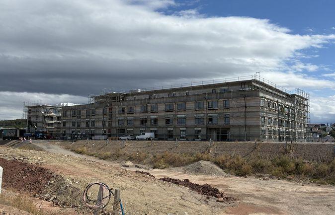 Mehrgeschossiger Neubau mit Gerüst auf einer Baustelle unter bewölktem Himmel.