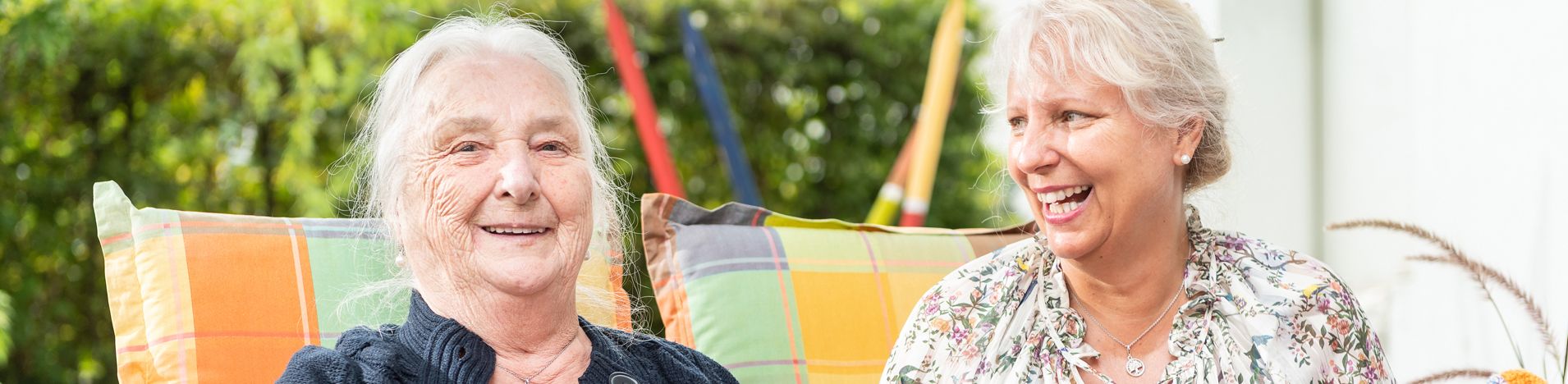 Ältere Frau beim Stricken und lachende Begleiterin mit bunter Decke