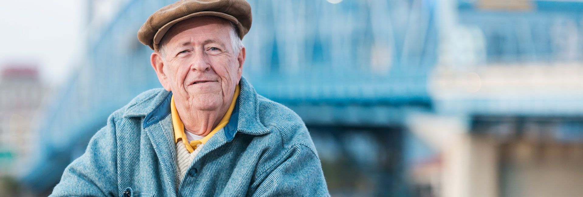 Älterer Mann mit Schirmmütze und blauer Jacke vor Brücke