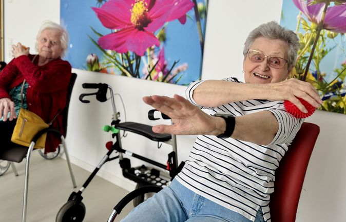 Ältere Frau massiert sich mit einem Massageball und lächelt dabei