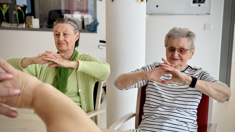 Zwei Damen sitzen auf einem Stuhl un machen Gymnastik