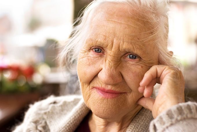 Nahaufnahme einer älteren Frau mit blauen Augen und Hand an der Wange