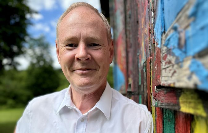 Porträt eines Mannes in weißem Hemd neben bunter Wand