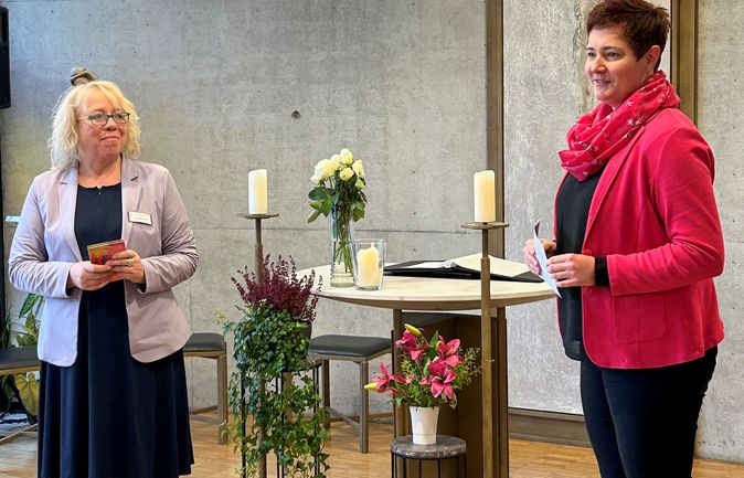 Zwei Frauen bei feierlicher Stabsübergabe vor Kerzen und Blumen