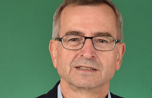 Mann mit Brille in Sakko und Hemd vor grünem Hintergrund