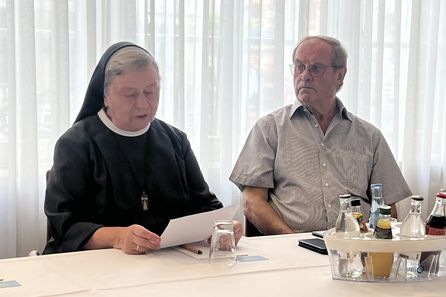 Ältere Ordensfrau liest Papier neben älterem Mann am Tisch
