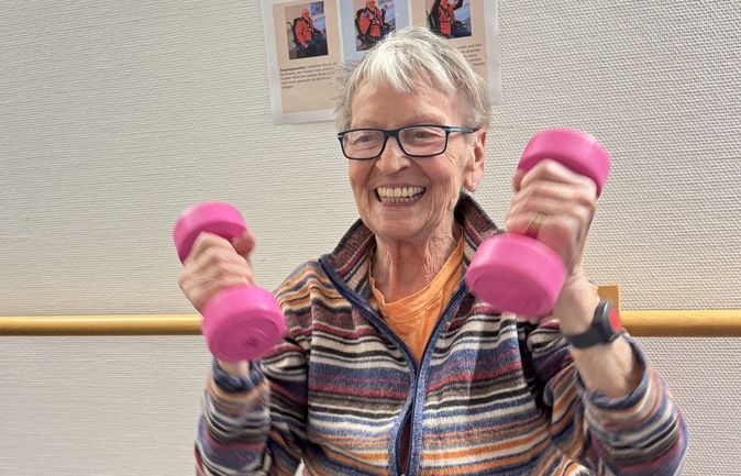 Seniorin hebt pinke Hanteln vor Trimm-mich-Pfad-Poster