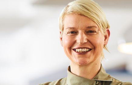Lächende Person mit kurzem blondem Haar und verschränkten Armen