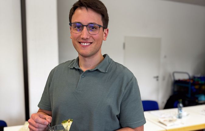 Person mit Brille hält grünen Smoothie mit Ananasstück in Kantine